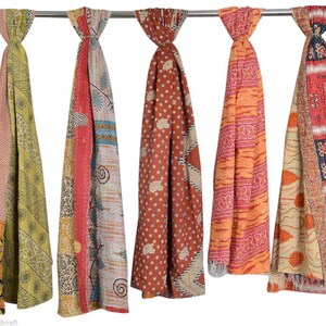 May include: Five colorful, patterned scarves hanging from a metal bar. The scarves display a variety of designs, including floral, geometric, and patchwork patterns. The color palette includes shades of red, orange, green, and brown.