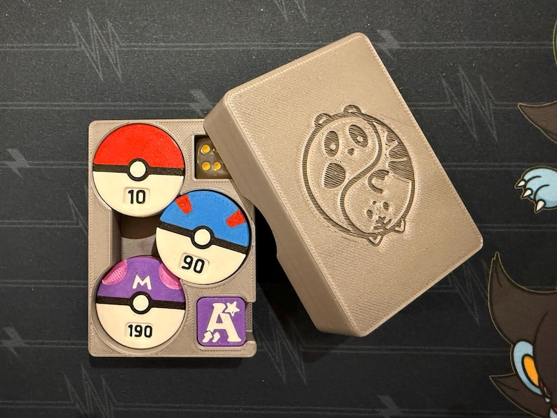 Pode incluir: Uma caixa de armazenamento cinza impressa em 3D com um design de panda yin-yang na tampa. Dentro h&aacute; tr&ecirc;s fichas circulares que lembram Pok&eacute; Balls com os n&uacute;meros 10, 90 e 190, uma ficha quadrada roxa com a letra A e um dado amarelo transl&uacute;cido.