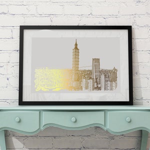 May include: A black framed print of a gold and black line drawing of a city skyline. The print is hanging on a white brick wall above a light blue dresser with three drawers.