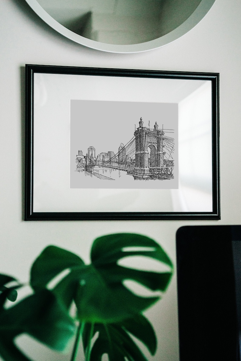 May include: A black and white line drawing of a bridge with a cityscape in the background. The drawing is framed in a black frame and hanging on a white wall.