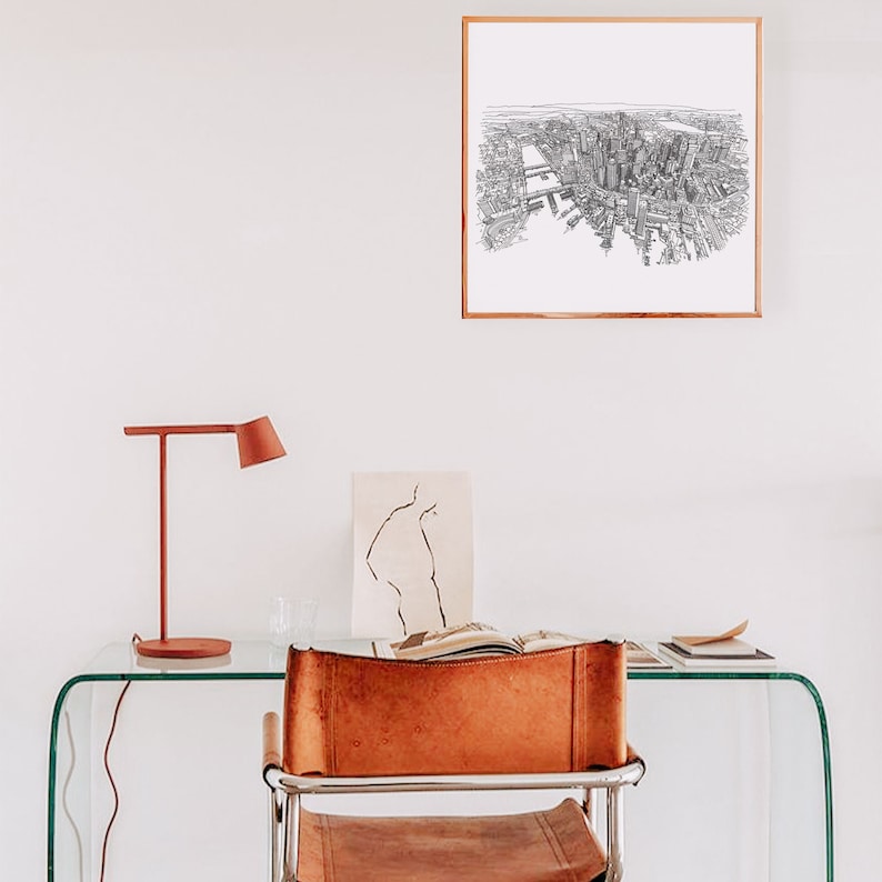 May include: A framed black and white line drawing of a city skyline with a river running through it. The drawing is hanging on a white wall above a glass desk with a brown leather chair and a red lamp.