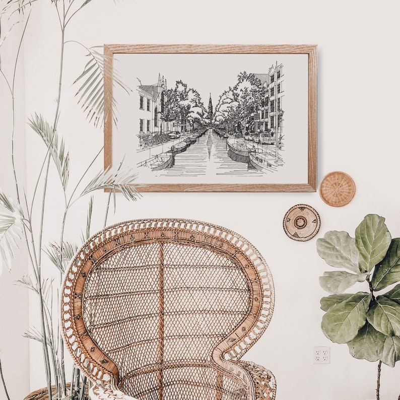 Puede incluir: Un dibujo en blanco y negro de una escena de canal con edificios y &aacute;rboles. El dibujo est&aacute; enmarcado y colgado en una pared blanca. Una silla de mimbre se encuentra frente a la obra enmarcada.