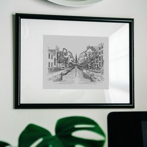 Puede incluir: Una impresi&oacute;n enmarcada en negro de un dibujo a l&iacute;nea de un canal en una ciudad. El canal est&aacute; bordeado de edificios y &aacute;rboles. Hay barcos en el canal.