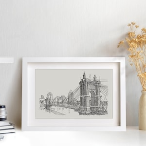 May include: Black and white line drawing of a suspension bridge with a cityscape in the background. The bridge is the focal point of the image, with the cityscape appearing in the distance. The drawing is framed in a white frame.
