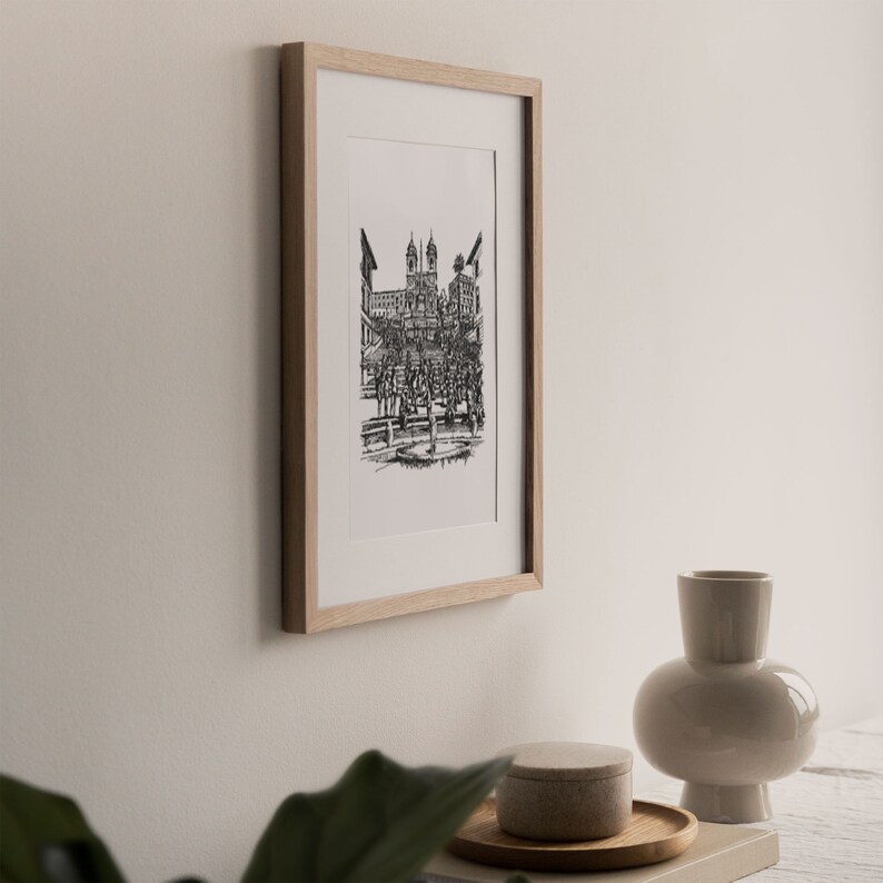 May include: A black and white line drawing of a city street scene with a church in the background, framed in a light wood frame.