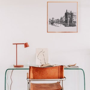 May include: A black and white line drawing of a bridge and cityscape hangs in a white room above a glass desk with a brown leather chair and a red lamp.