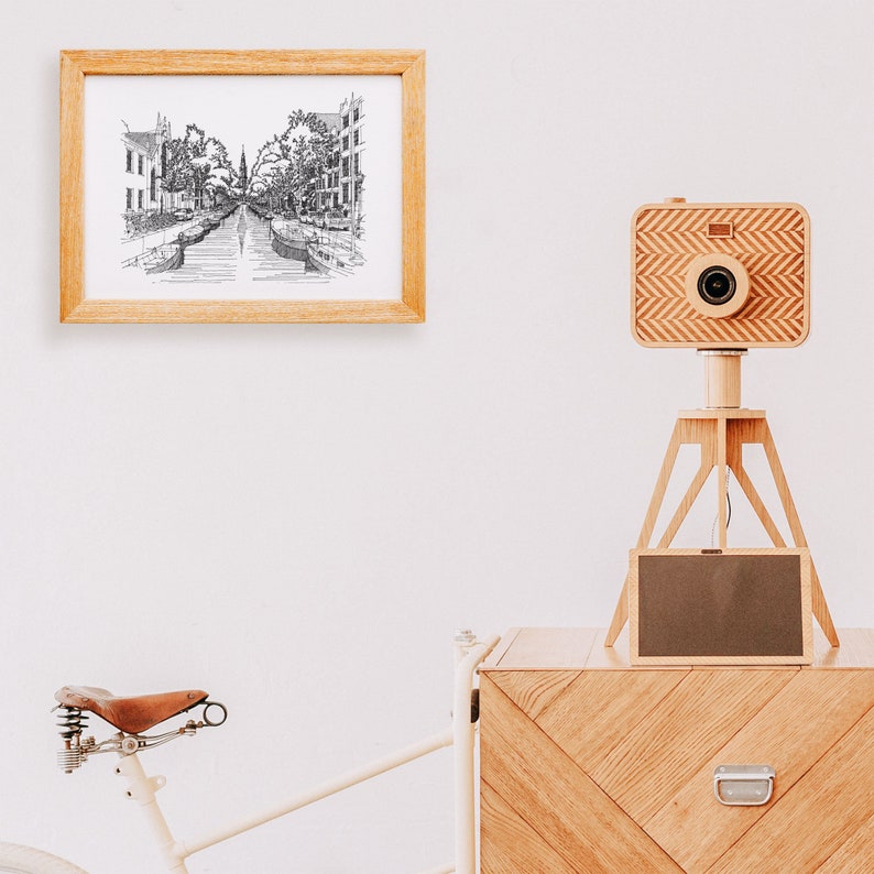 Puede incluir: Una c&aacute;mara de madera en un tr&iacute;pode con una pantalla negra, un dibujo en blanco y negro enmarcado de un canal y una c&oacute;moda de madera con un caj&oacute;n.