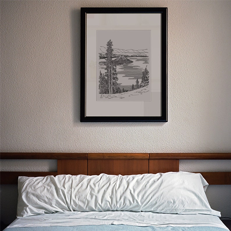 May include: A black framed print of a line drawing of a lake with an island in the middle, surrounded by trees. The print is hanging on a wall above a bed with a white headboard.
