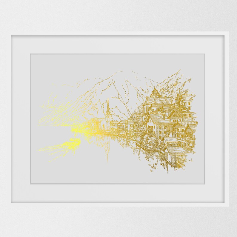 May include: A framed art print featuring a gold-toned illustration of a lakeside village with mountains in the background. The artwork has a detailed, sketched style, with a bright yellow and gold gradient effect on the left side. The print is set in a white frame.