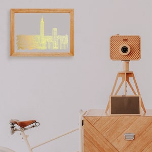 May include: A wooden camera on a tripod with a black screen, a framed print of a gold city skyline, and a brown leather bicycle seat.