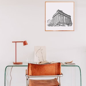May include: A framed black and white architectural print of a classical building hangs on a white wall. A red desk lamp and a leather chair are in front of a glass desk. A drawing and an open book are on the desk.