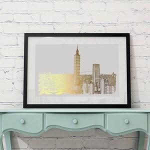 May include: A black framed print of a gold and black line drawing of a city skyline. The print is hanging on a white brick wall above a light blue dresser with three drawers.