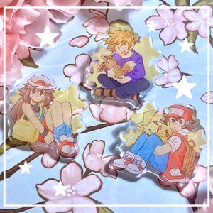 May include: Three cartoon character charms featuring a girl with brown hair and a red hat, a boy with brown hair and a red hat, and a boy with blonde hair. Each charm has a yellow starburst background and a sparkly finish.