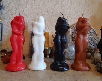 Op de afbeelding: Vier gebeeldhouwde kaarsen in de vorm van twee figuren die elkaar omhelzen. De kaarsen zijn rood, wit, zwart en bruin.