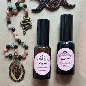 Puede incluir: Dos botellas de vidrio marrón con tapas negras y etiquetas rosas que dicen "Hécate Brume Naturelle MyTimeco" en texto negro. Las botellas están sobre una superficie marrón claro.