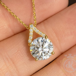 Könnte beinhalten: Eine goldene Halskette mit einem großen, runden, klaren Edelsteinanhänger. Der Anhänger ist in Gold mit kleinen, klaren Steinen gefasst. Die Kette ist ebenfalls aus Gold.