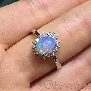 May include: A silver ring featuring a large oval opal gemstone set in a halo of smaller clear stones.