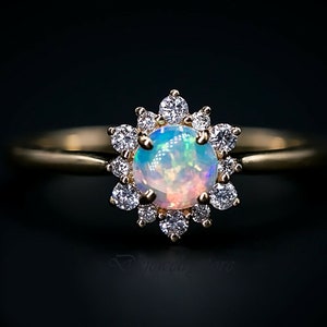 Könnte beinhalten: Ein goldener Ring mit einem großen Opal-Edelstein, der von einem Heiligenschein aus kleineren Diamanten umgeben ist.