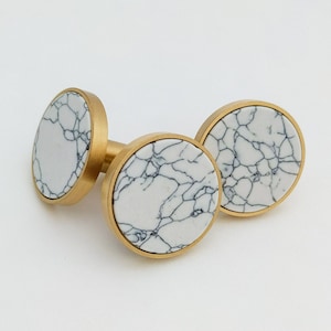 May include: Two round, gold-toned cabinet knobs with white marble-like inlays. The knobs have a smooth, polished finish.
