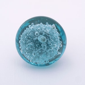 May include: A blue glass paperweight with a cluster of air bubbles inside.
