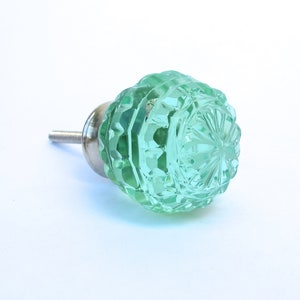 May include: A light green glass cabinet knob with a faceted design and a silver metal stem.