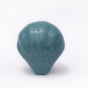 May include: A teal blue ceramic knob with a crackled finish. The knob is round and has a slightly irregular shape.
