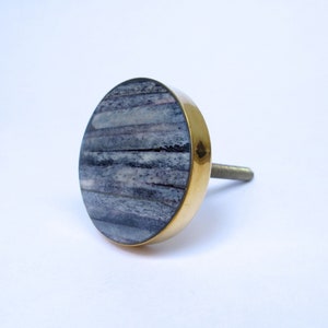May include: A round cabinet knob with a brass rim and a gray and white striped face. The knob has a threaded post for easy installation. This decorative hardware is perfect for updating furniture.