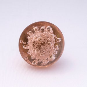May include: A round, clear glass paperweight with a pink hue and many small air bubbles trapped inside.