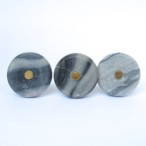 May include: Three gray marble cabinet knobs with brass center accents. The knobs have a circular shape and a natural stone pattern. These decorative knobs are ideal for adding a touch of elegance to furniture or cabinetry.