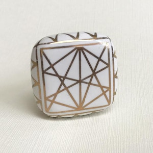May include: White ceramic cabinet knob with a gold geometric design.