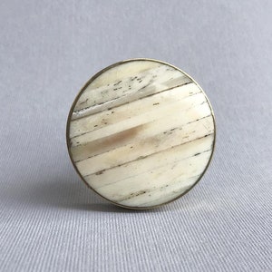 May include: A round, white and brown, bone inlay cabinet knob with a brass rim.