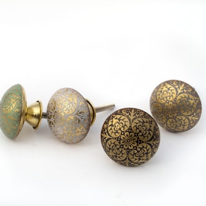 May include: Decorative cabinet knobs in various colors. One knob is mint green with gold accents, another is white with gold floral patterns, and two are dark brown with gold floral patterns. The knobs have a round shape.