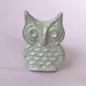 May include: White ceramic owl figurine with a blue glaze. The owl has large, round eyes and a textured body.