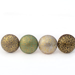 May include: Four decorative cabinet knobs in a row. Each knob is round with a floral pattern in gold. The knobs are in shades of brown, green, and gold, with a white background.