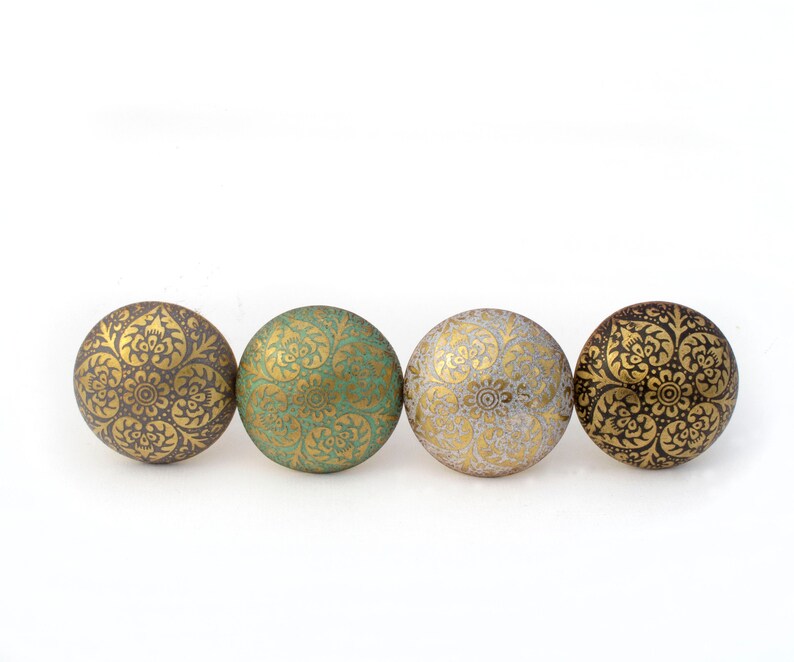 May include: Four decorative cabinet knobs in a row. Each knob is round with a floral pattern in gold. The knobs are in shades of brown, green, and gold, with a white background.