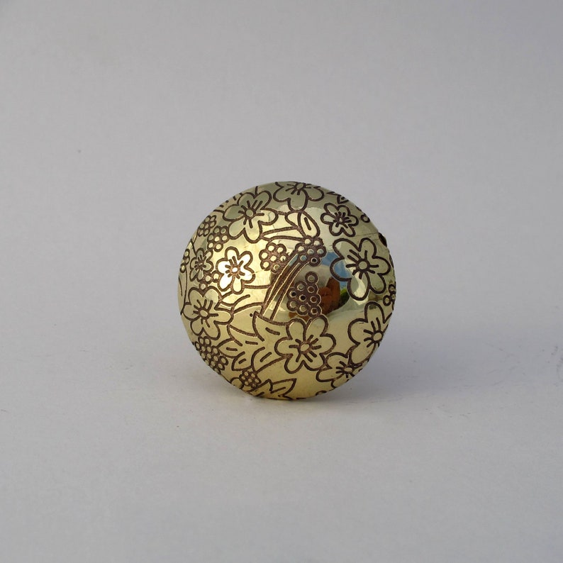May include: A gold-colored round knob with a floral design. The knob has a raised pattern of flowers and leaves.