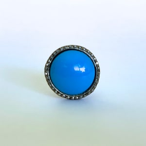May include: A turquoise blue cabochon ring with a silver setting. The ring has a round bezel setting and a smooth, polished finish.