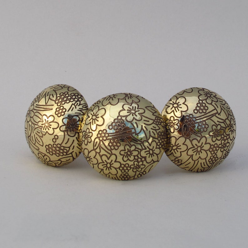 May include: Three gold-colored round ornaments with a floral pattern. The ornaments are arranged in a row.