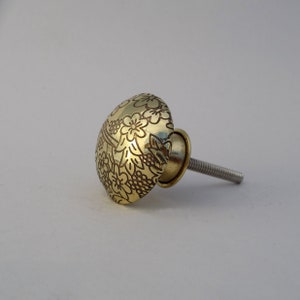 May include: A gold-toned cabinet knob with a floral design. The knob has a screw-on stem.