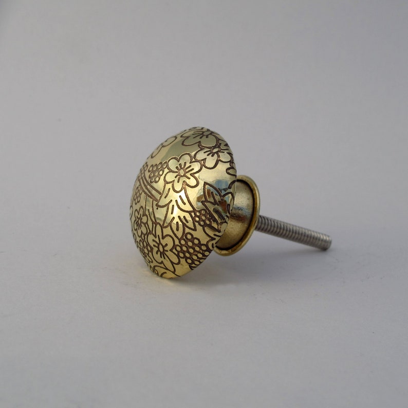 May include: A gold-toned cabinet knob with a floral design. The knob has a screw-on stem.
