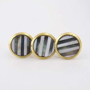 May include: Three round, gold-toned cabinet knobs with a black and white striped mother-of-pearl inlay.