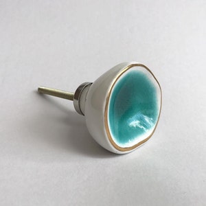 May include: White ceramic cabinet knob with a teal blue center and a gold rim.