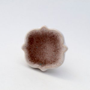May include: A white ceramic cabinet knob with a brown center and a decorative, scalloped edge.