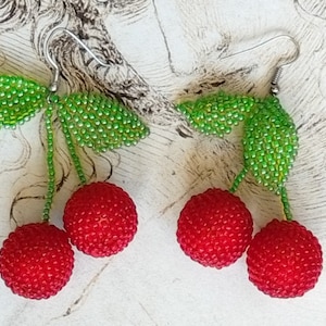 May include: A pair of beaded cherry earrings with green leaves. The cherries are red and the leaves are green.