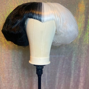 May include: A black and white wig with a straight, blunt cut. The wig is styled with a center part and is split down the middle, with one side black and the other side white.