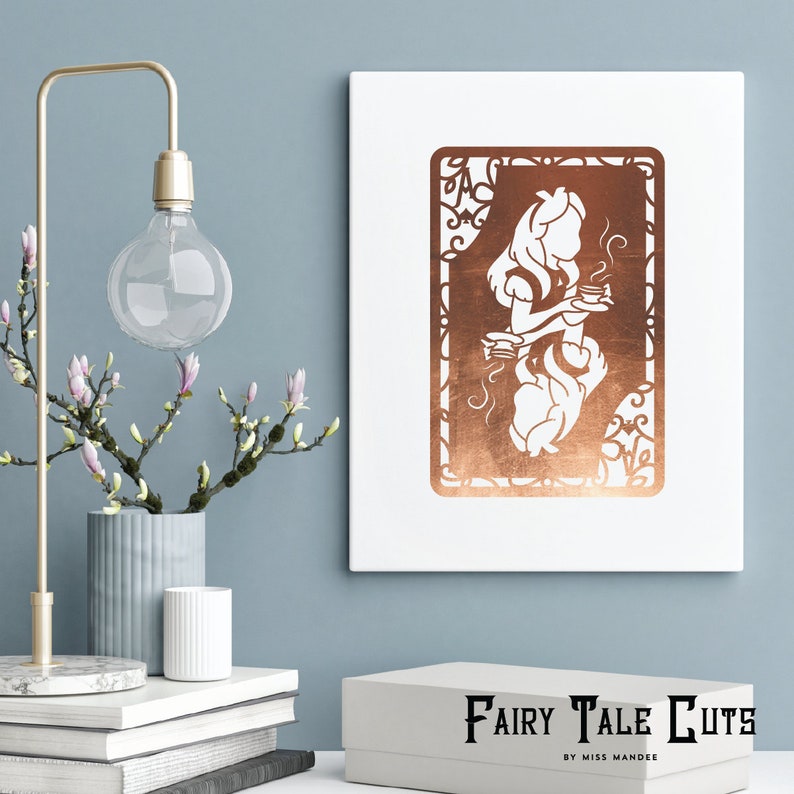 May include: A copper-colored silhouette of Alice from Alice in Wonderland holding a teacup, framed with a decorative border. The image is on a white canvas with the text "Fairy Tale Cuts by Miss Mandee" below.