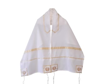 Puede incluir: Chal de oración blanco con ribete dorado y diseños decorativos en las esquinas. El chal tiene forma rectangular con una abertura central para la cabeza y largas borlas colgantes.