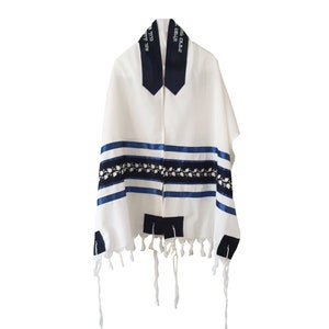 May include: White prayer shawl with blue stripes and decorative black and white floral pattern. The shawl has dark blue accents at the neck and corners, with Hebrew text. Measures 20 inches x 72 inches.