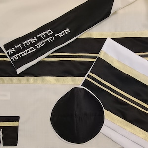 May include: A white and black prayer shawl with gold trim and Hebrew text. The set includes a black kippah and a small black pouch with gold trim. The shawl has black stripes and gold accents.