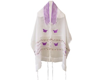 May include: White prayer shawl with purple details and butterfly motifs. The shawl has a purple collar with Hebrew text and a floral and ribbon design. The shawl has four tassels hanging from the bottom.